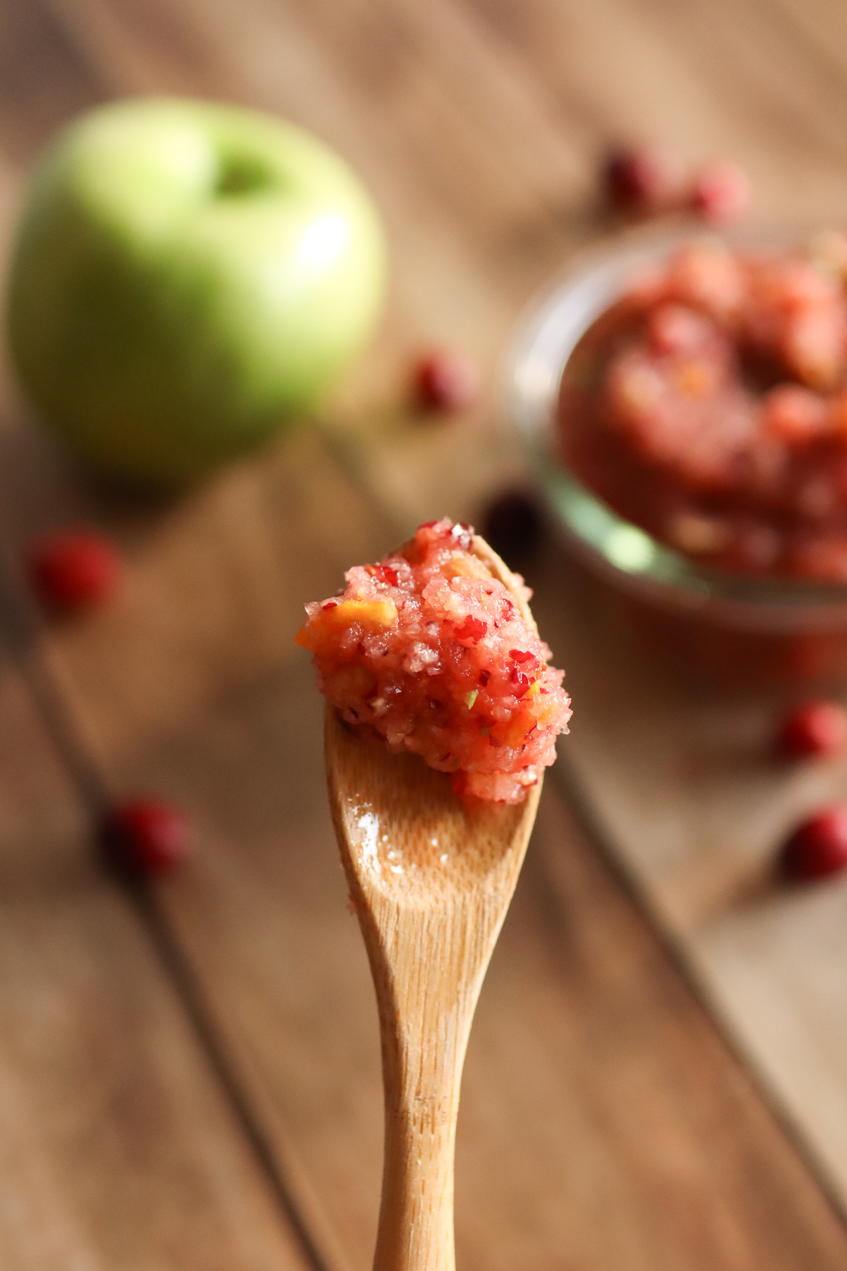 A spoonful of cranberry relish with an apple and a bowl of relish in the background.