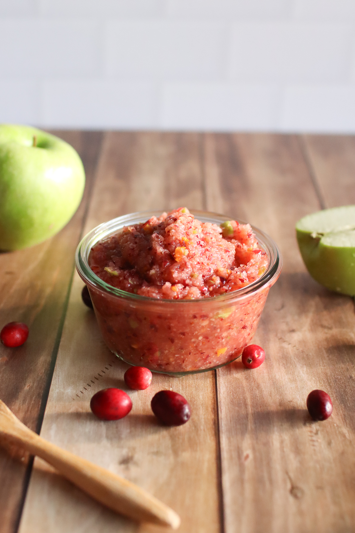 A jar of cranberry relish with apples, cranberries, and a spoon.