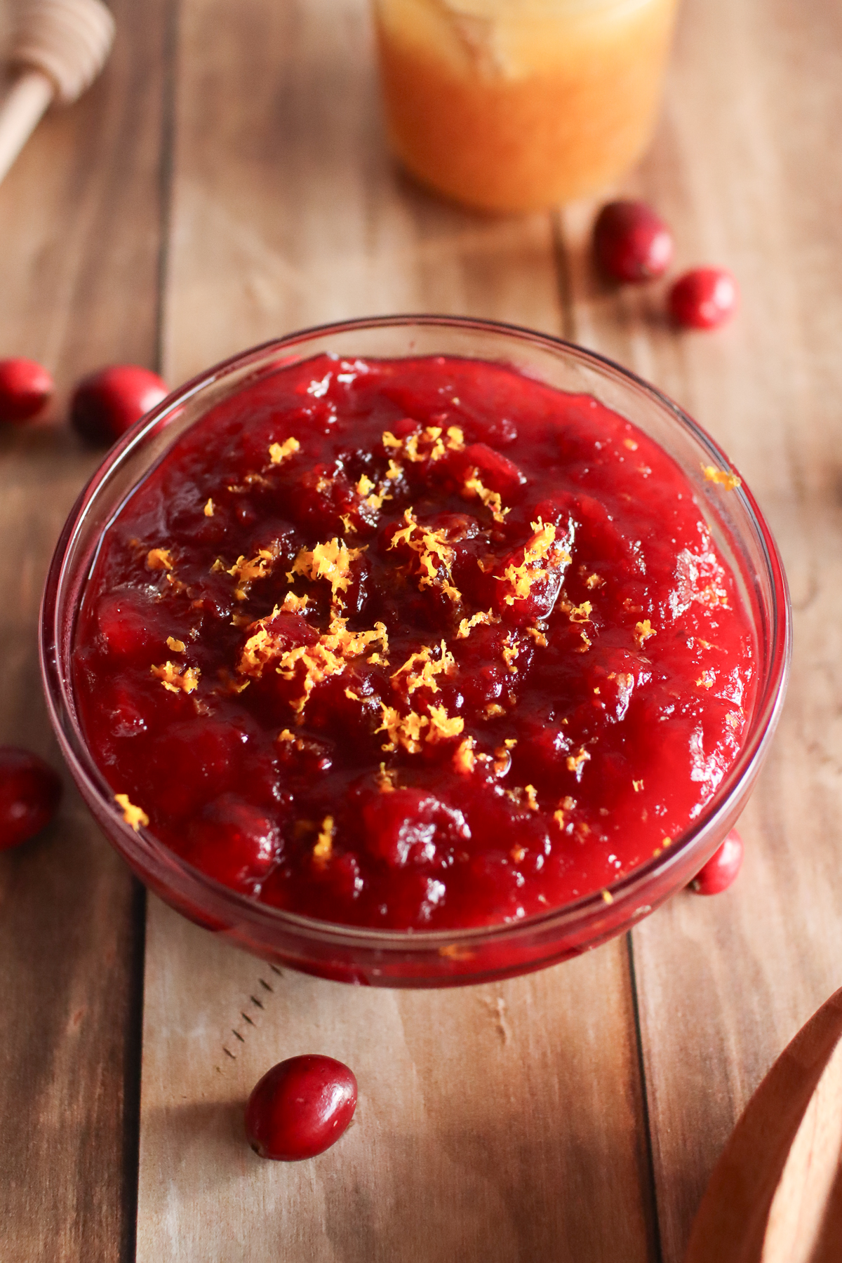 A bowl of cranberry sauce with fresh cranberries and a jar of honey.