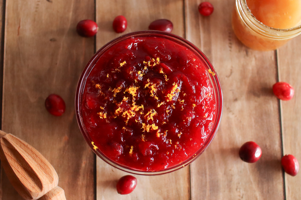 A bowl of cranberry sauce with cranberries and honey next to it.