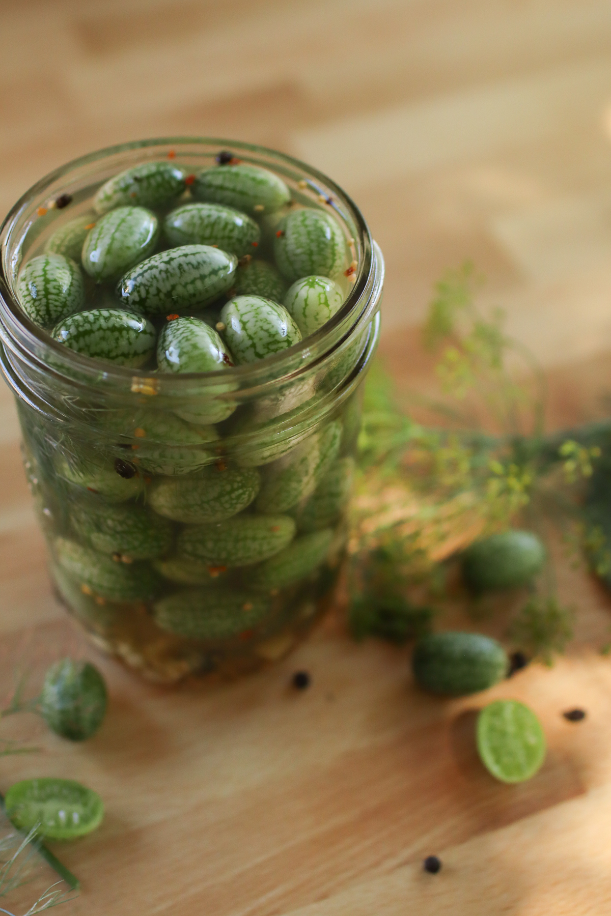 A jar of cucamelon pickles with cucamelons and dill on the table around it. 