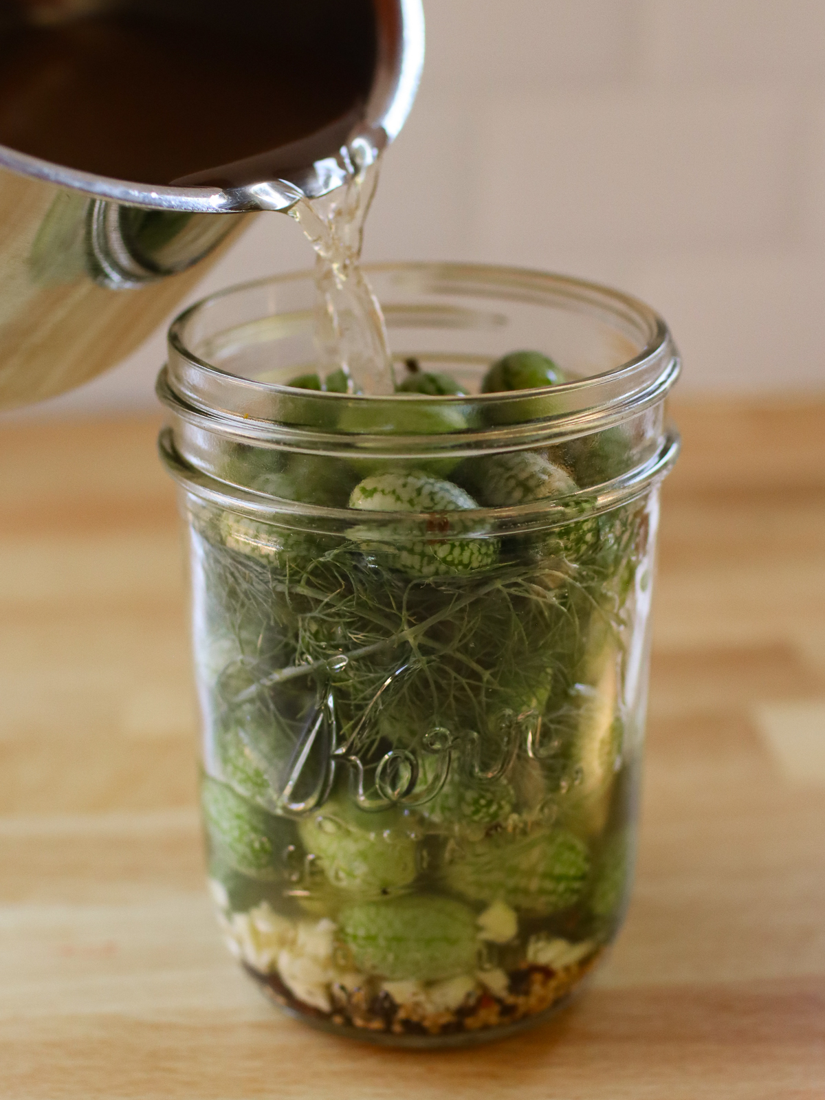 Pouring pickle brine into a jar of cucamelons.