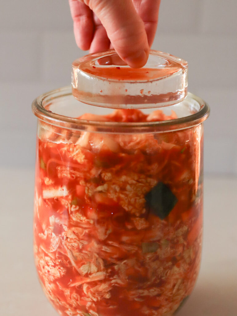 Kimchi in a jar with a glass weight being set on top. 